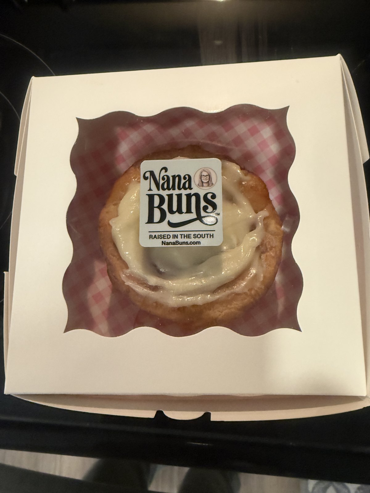 A frosted Nana Bun in a box with the Nana Buns label