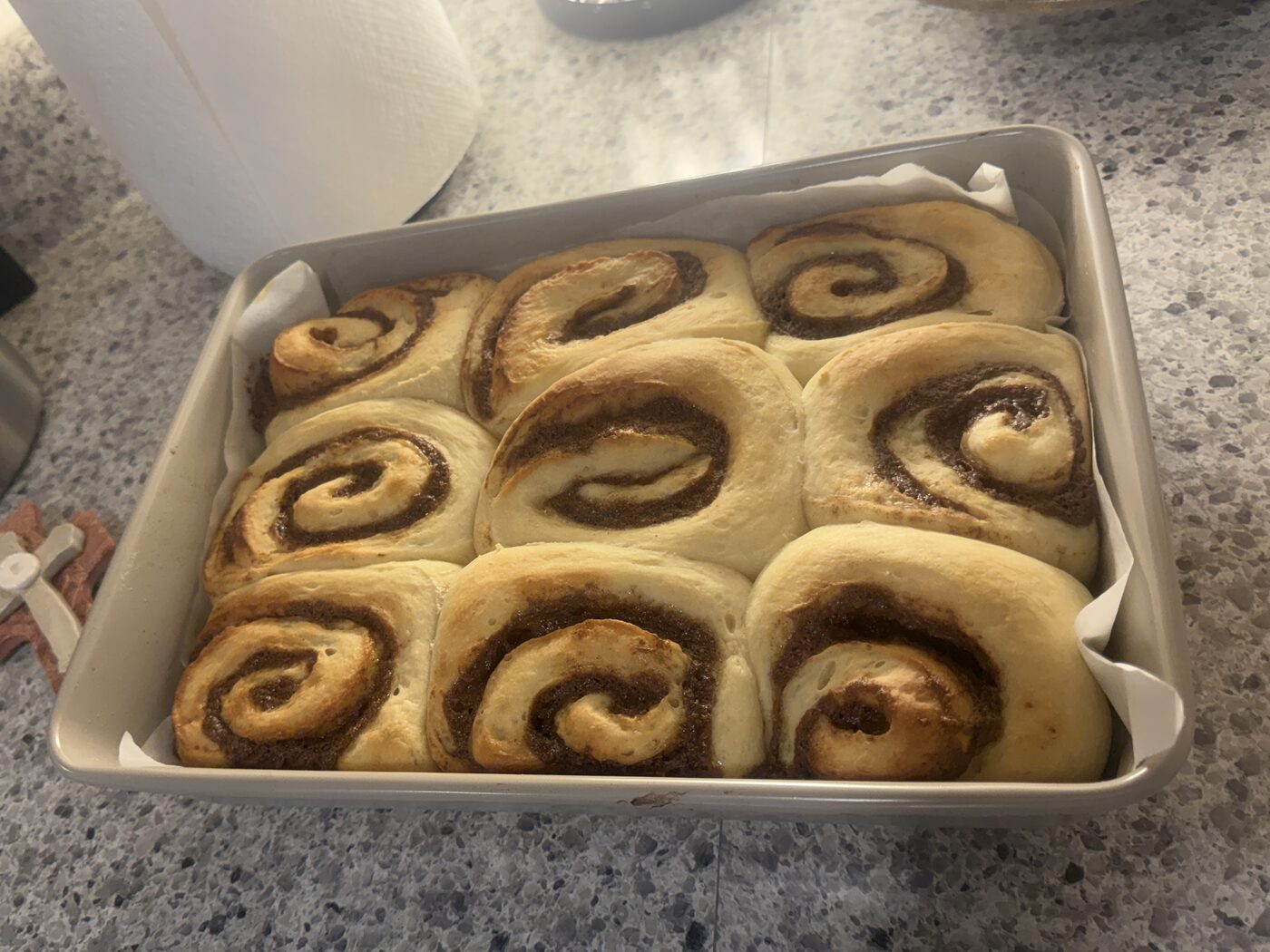 Nine cinnamon buns risen and plump in a parchment-lined pan, ready for the oven