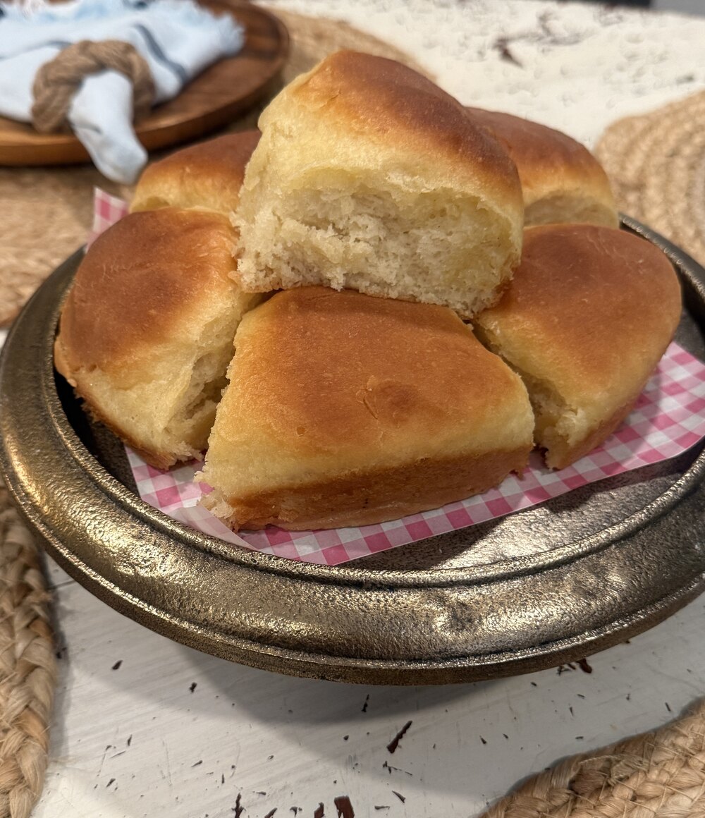 Golden pull-apart Mawmaw’s yeast rolls in a brass footed dish on pink gingham